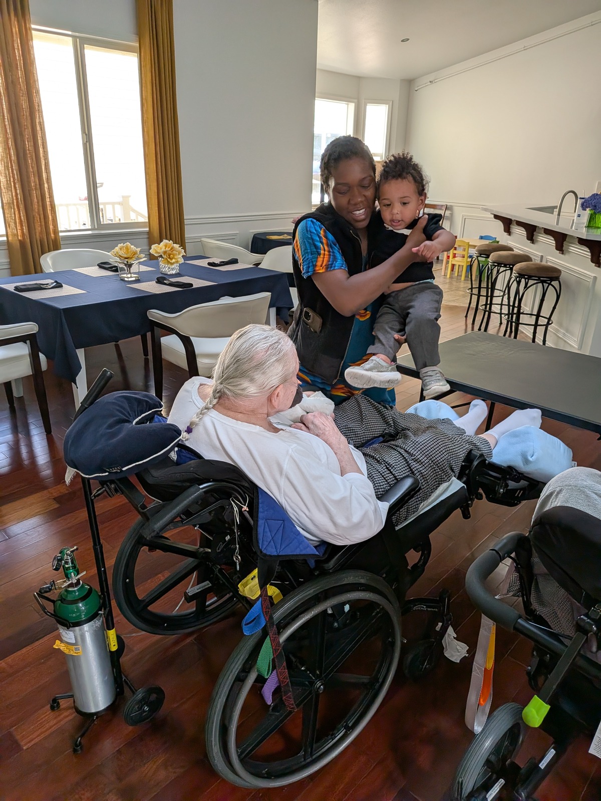 Toddler visiting elderly resident in wheelchair at Edmonds Villa — intergenerational connection and family involvement